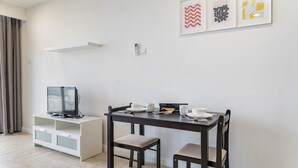 A modern living room with a dark wooden table, two chairs, a white cabinet, and a flat-screen TV. - OYO Home 44050 Essential Studio Empire Marriot (Petaling Jaya)