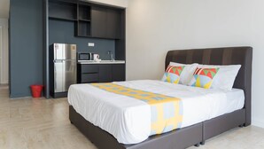 A modern hotel room with a bed, a built-in kitchen area, and a red trash bin. - OYO Home 44050 Essential Studio Empire Marriot (Petaling Jaya)