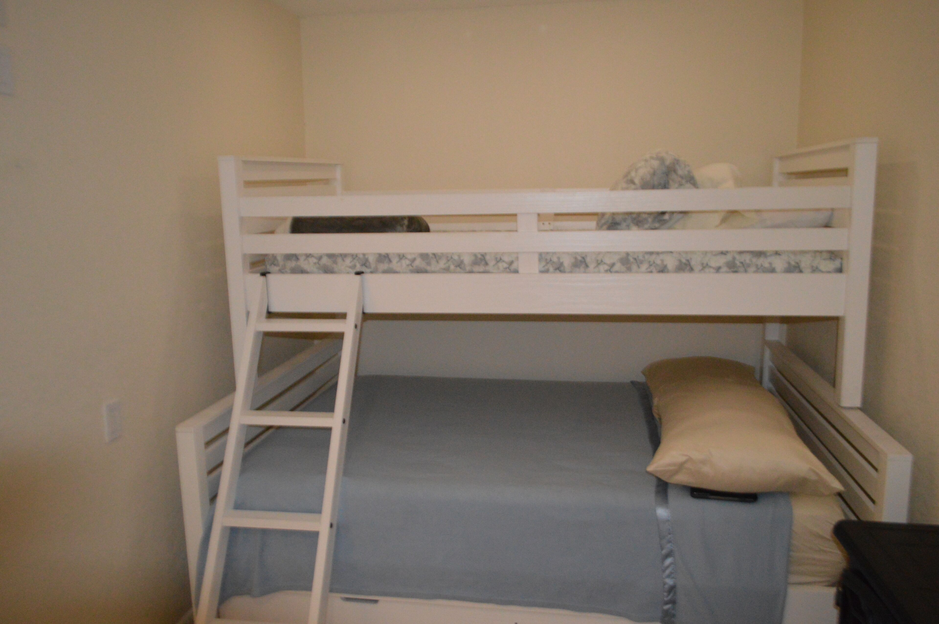 A bunk bed with a ladder, a single bed below, and a small desk.