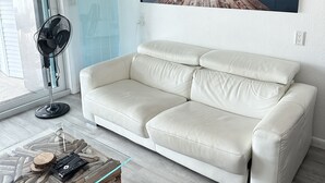 A modern living room with a white leather sofa, a glass coffee table with a wooden base, and a large landscape painting on the wall. - Dream Vacation Home Key Colony Beach Marathon Now with private pool! (Marathon)
