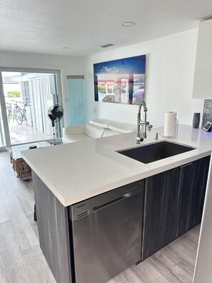 A modern kitchen with a stainless steel dishwasher, a large island with a sink, and a view of the outdoors through a glass door. - Dream Vacation Home Key Colony Beach Marathon Now with private pool! (Marathon)