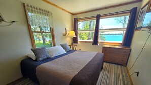 Ein Schlafzimmer mit einem großen Bett, einem Schminktisch, einer Lampe und Blick ins Freie.