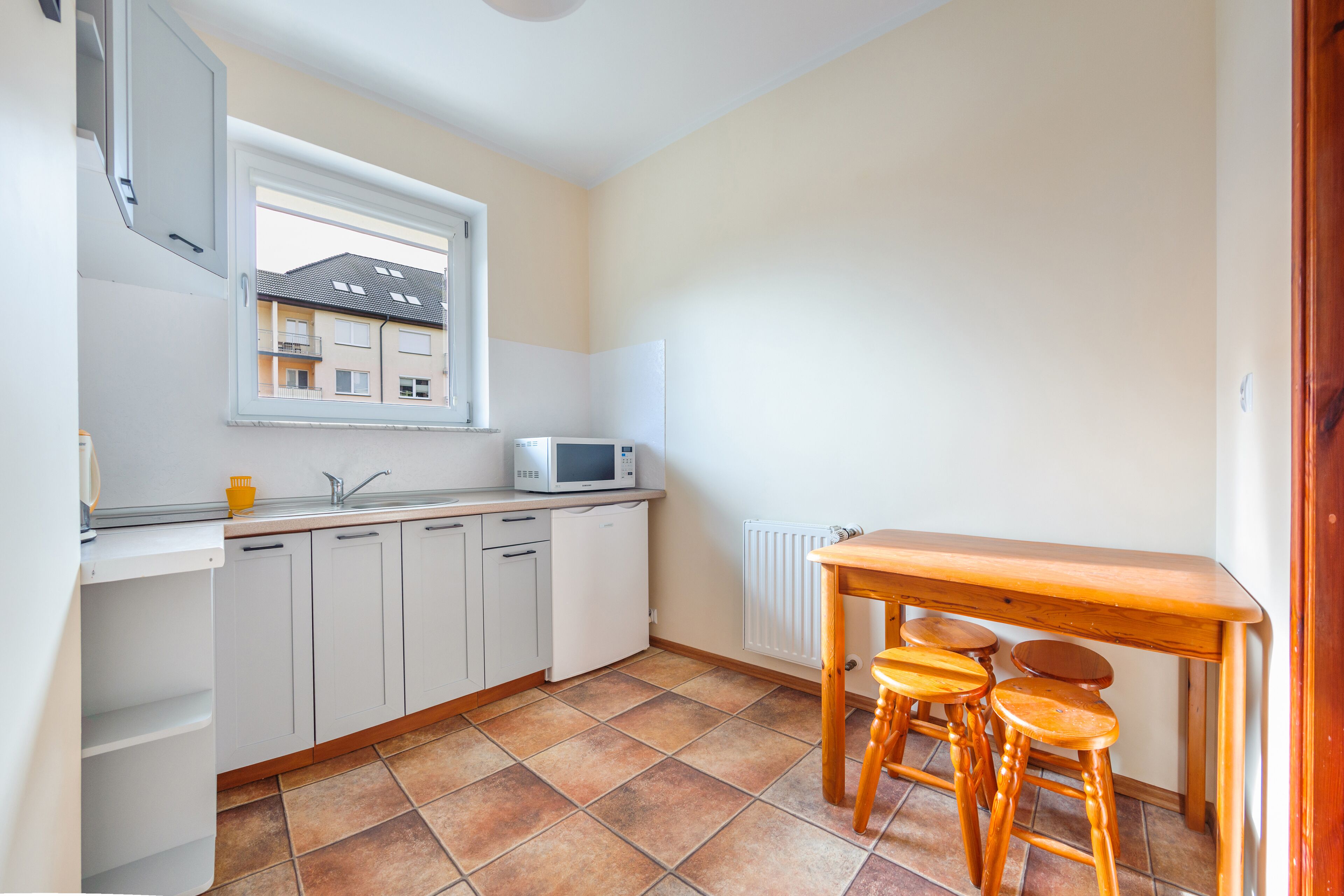 Una cocina compacta con armarios blancos, microondas, pileta y una mesa de madera con taburetes.