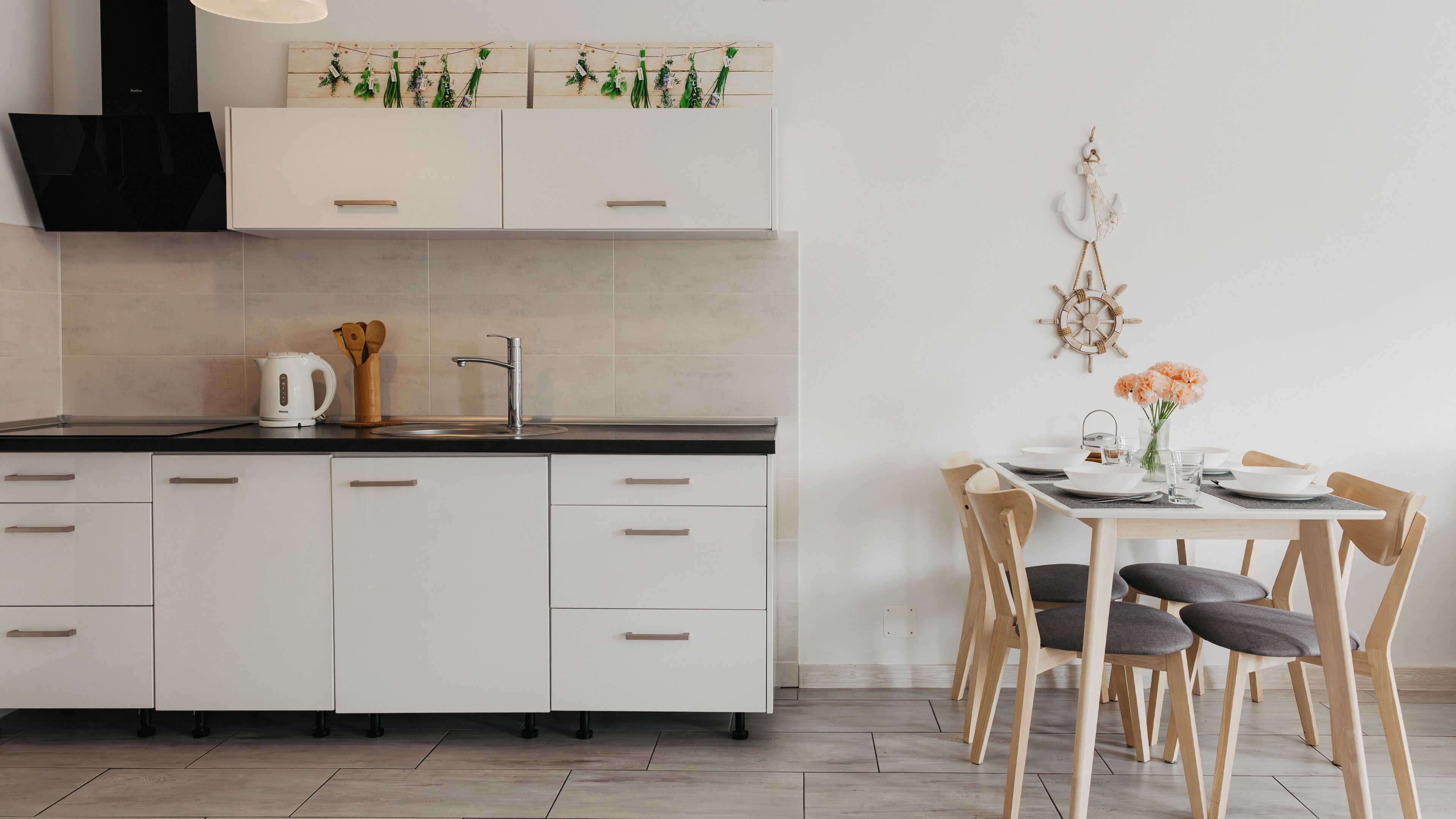 A modern kitchen with white cabinets, a black countertop, and a dining area with wooden chairs and a table set for two.