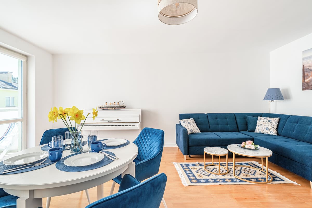 A modern living room with a blue sofa, a dining table set with blue tableware, and a painting on the wall.