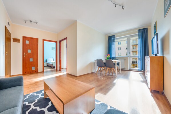 A modern living room with a wooden coffee table, a grey sofa, and a dining area with a table and chairs. - Sun & Snow Na Wydmie (Ustka)