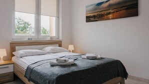 Een net opgemaakt bed met een grijze deken, twee bedlampen en een schilderij van een zonsondergang aan de muur.