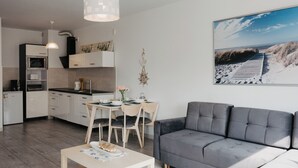 Een moderne keuken met witte kasten, een zithoek met een tafel en stoelen, en een grijze bank.