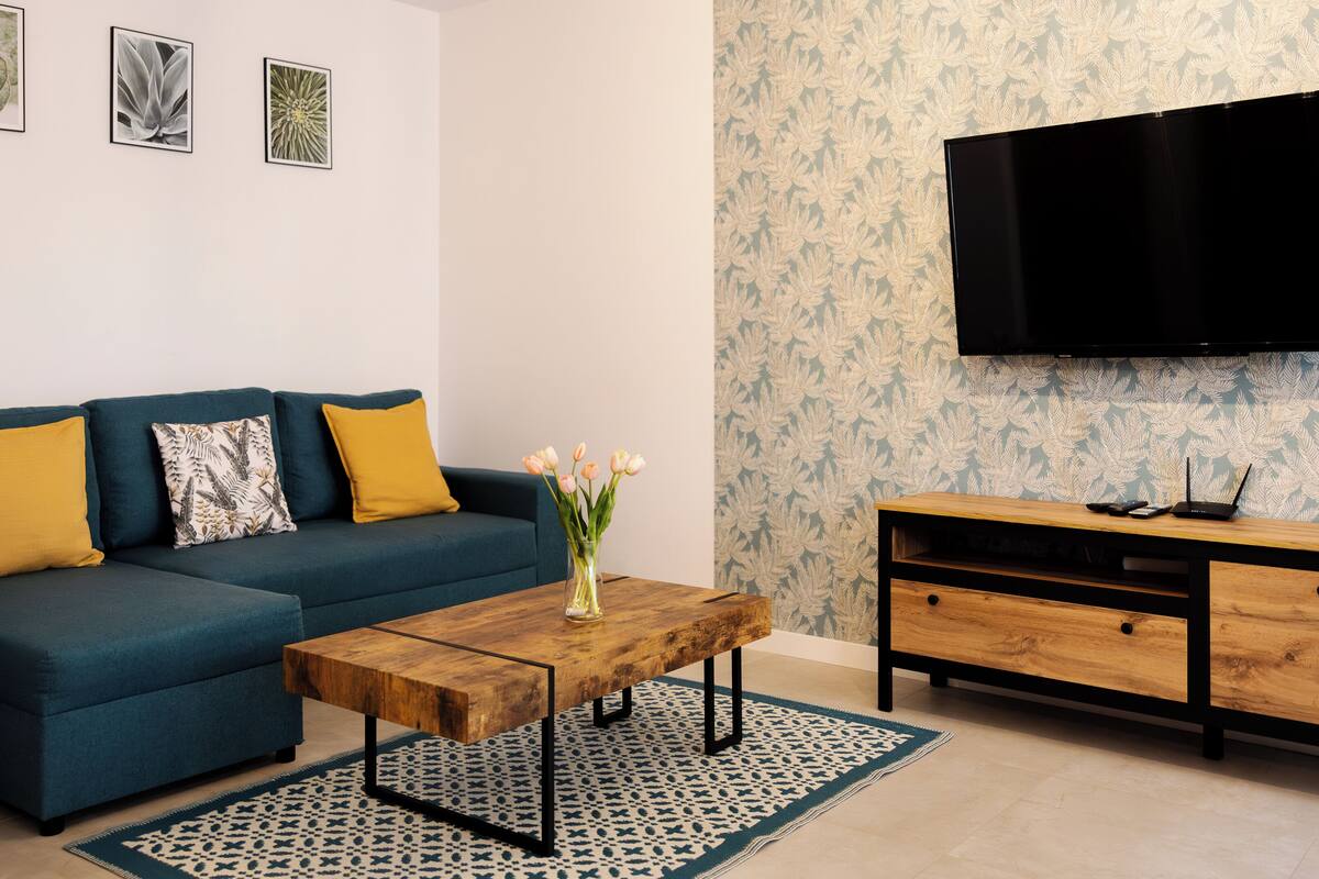 A modern living room with a blue sofa, a wooden coffee table, and a TV mounted on the wall.