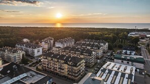 Een woonwijk met meerlaags appartementencomplexen, een parkeerplaats en uitzicht op zee bij zonsondergang.