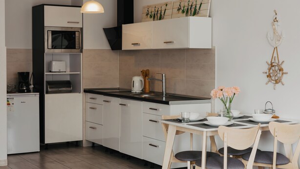 Een moderne keuken met witte kastjes, een ingebouwde oven en een eethoek met een tafel en stoelen.