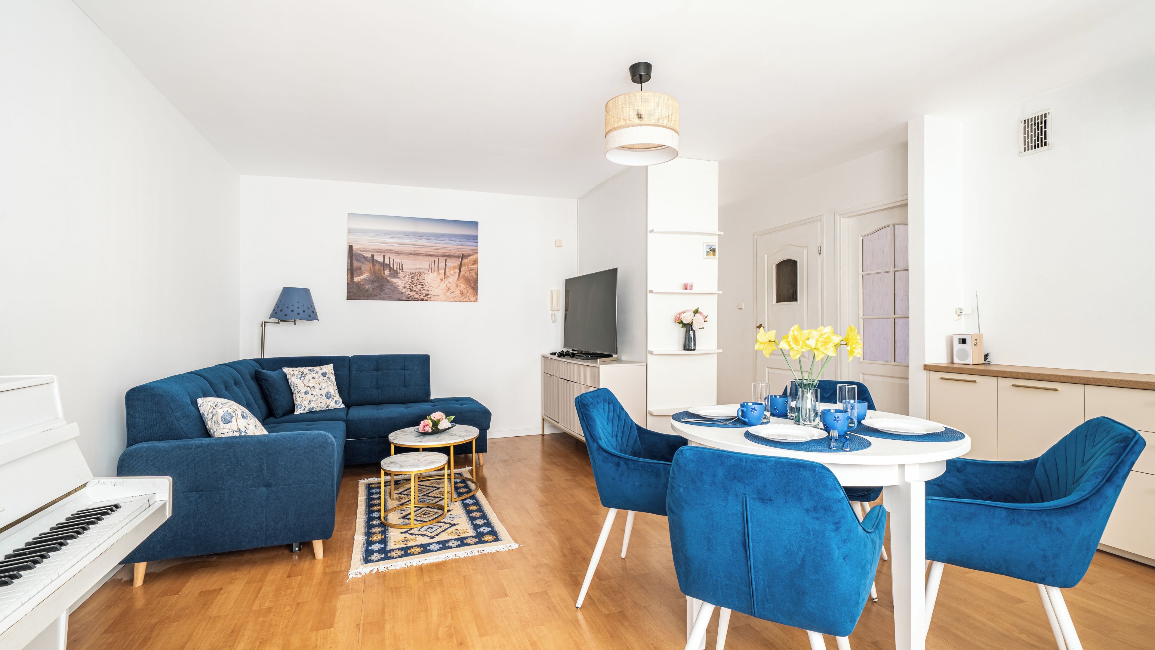 A modern living room with a sofa, a dining table with chairs, a TV, and a piano.