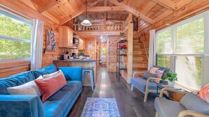 Un interior acogedor de cabaña con un sofá azul, un pequeño comedor y una cocina.
