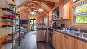 Interior de una cabaña de madera con cocina, comedor y vistas al exterior.