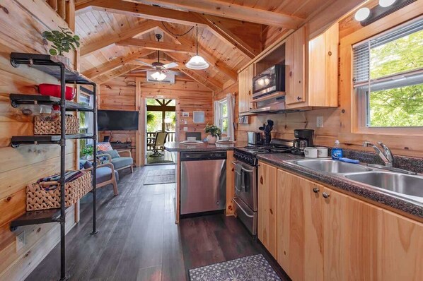 A wooden cabin interior with a kitchen, dining area, and a view of the outdoors.