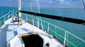 Il ponte di una barca a vela con vista sull'oceano e una costa in lontananza.