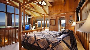 A wooden cabin bedroom with a large bed, a TV, and a balcony with a view of the mountains. - AWESOME VIEW! 1 bedroom, sleeps 2! (Sevierville)