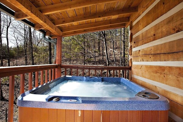 Un jacuzzi en una cabaña de madera con terraza de madera y vista al bosque.
