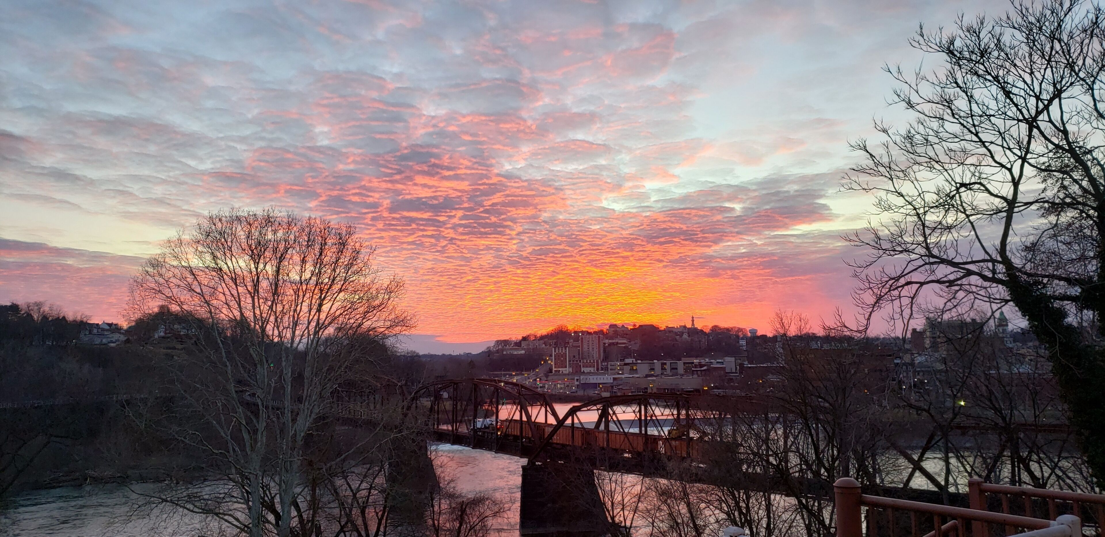 A sunset over a river with a bridge and buildings in the background.