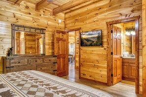 L’intérieur d’une cabane en rondins, avec un lit, une commode et un tableau représentant un paysage de montagne.