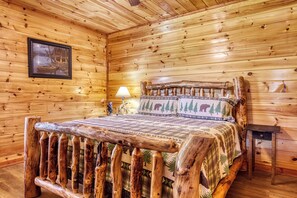 Interior de una cabaña de madera con una cama, un cuadro en la pared y una lámpara.