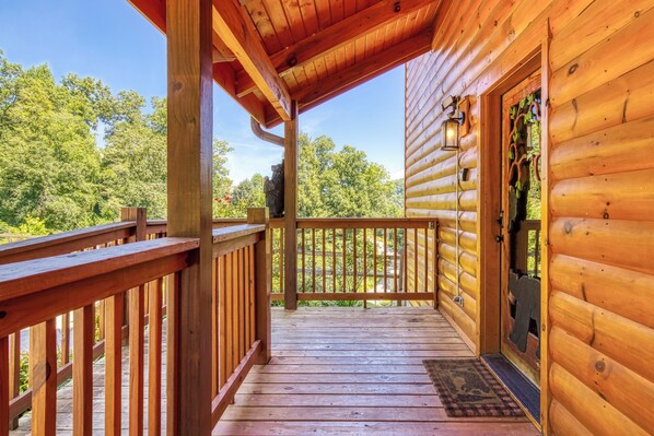 Une terrasse en bois avec une rambarde, une porte dotée d’une fenêtre et une vue sur les arbres.