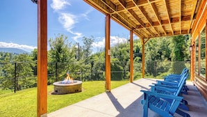 A covered outdoor area with a fire pit, seating, and a view of a mountain. - Luxury 5BR Cabin w/ Private Pool, Firepit, Theater & Game Room – In Gatlinburg (Gatlinburg)