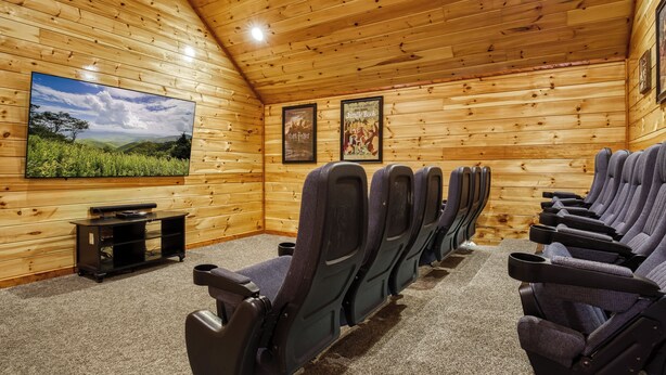 A wooden-paneled room with a row of seats, a television, and two posters on the wall. - Luxury 5BR Cabin w/ Private Pool, Firepit, Theater & Game Room – In Gatlinburg (Gatlinburg)