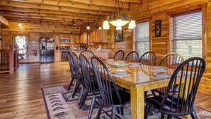 A wooden cabin interior with a dining area, kitchen, and a large window. - Luxury 5BR Cabin w/ Private Pool, Firepit, Theater & Game Room – In Gatlinburg (Gatlinburg)