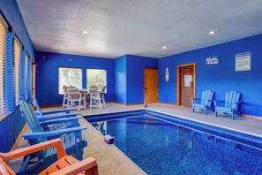 Une piscine intérieure aux murs bleus et au plafond bleu, entourée de chaises Adirondack bleues et orange.