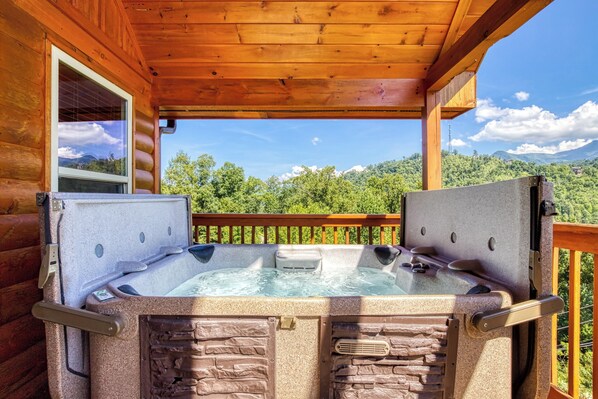 A wooden cabin with a hot tub and a window overlooking a forested mountain.