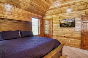 Une chambre dans une cabane en bois, avec un lit, une fenêtre avec des stores, une porte et un téléviseur fixé au mur.