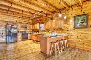 Un interior de madera con una cocina que cuenta con un refrigerador de acero inoxidable, un microondas y una estufa. Hay taburetes de madera en la isla de la cocina.