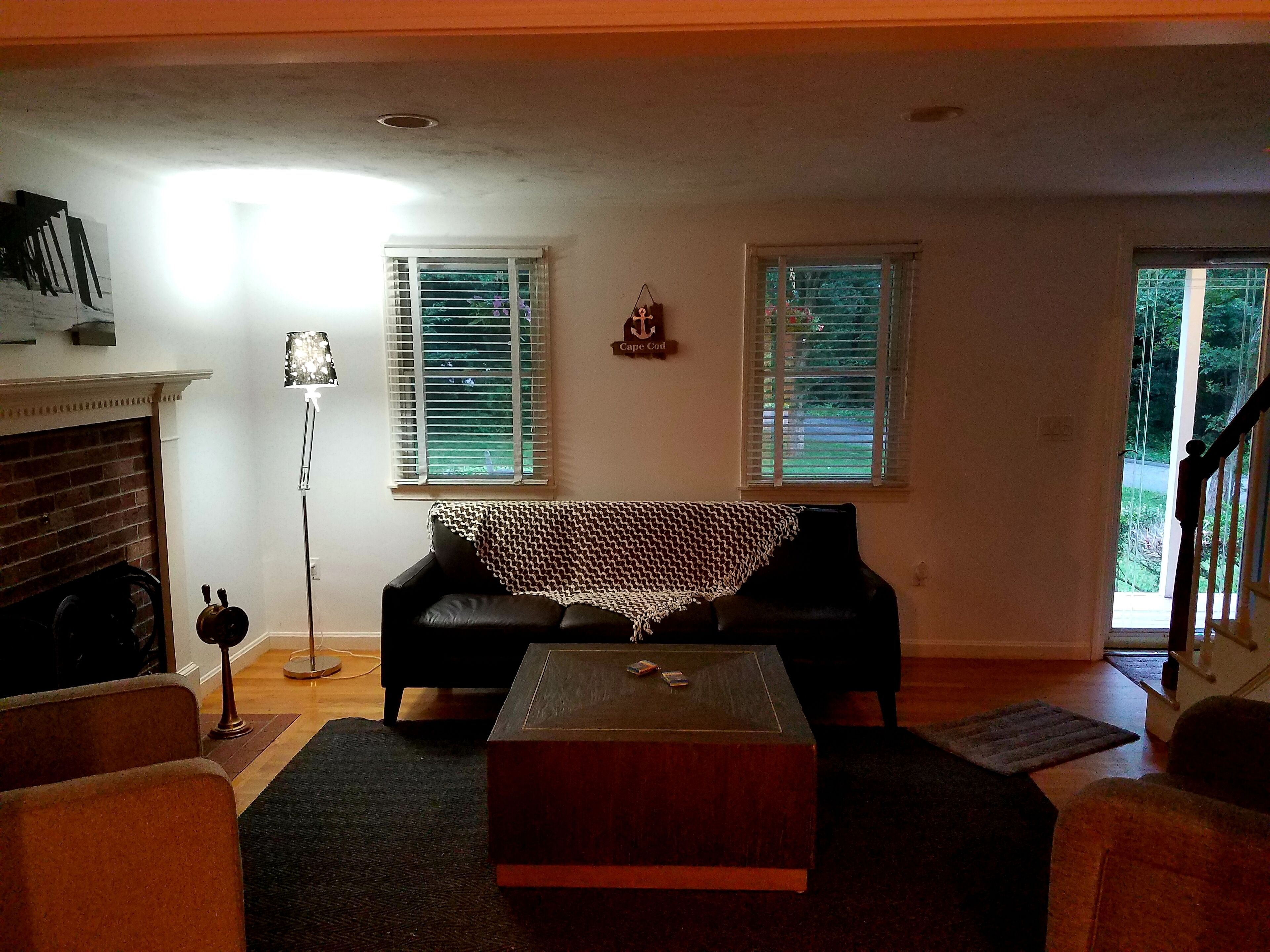 A living room with a fireplace, two windows with blinds, a black sofa, a wooden coffee table, and a floor lamp.
