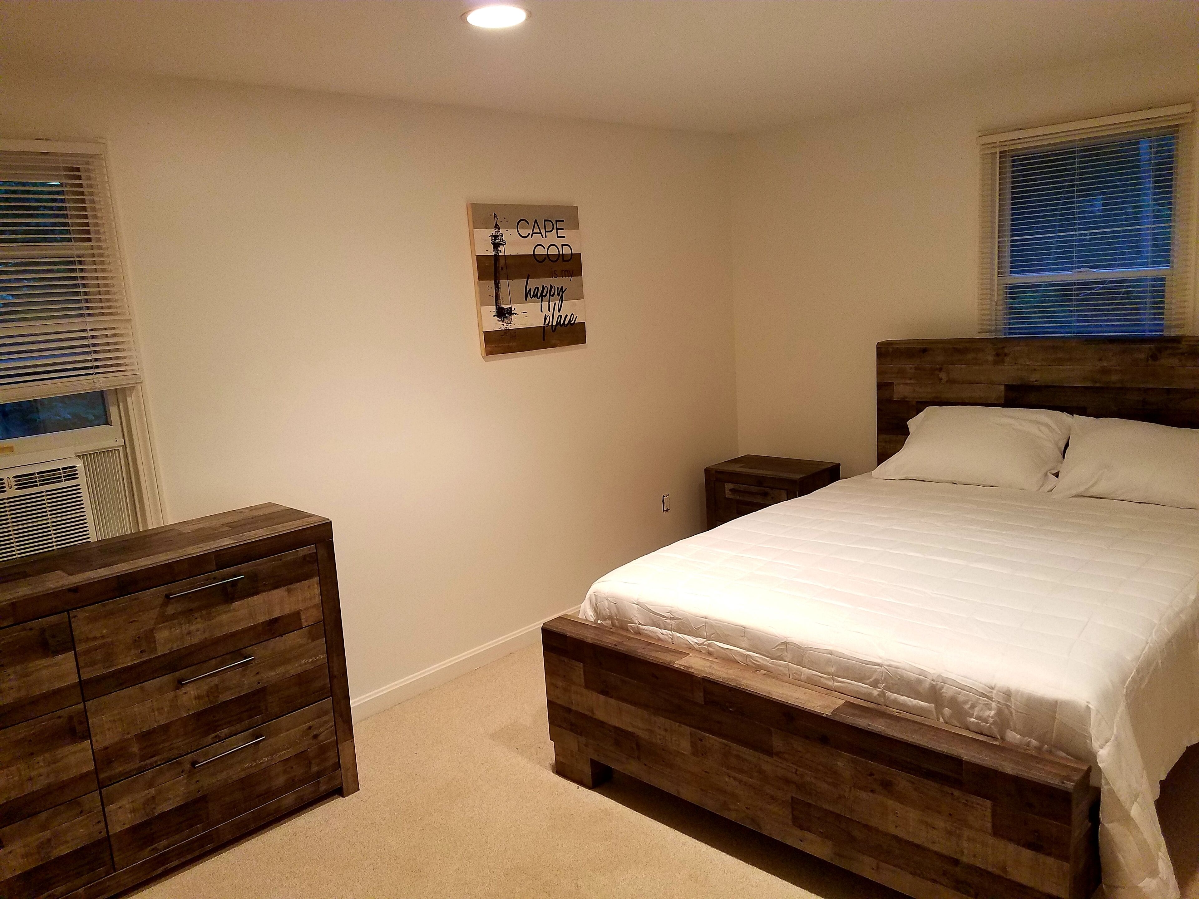 A bedroom with a wooden bed, a nightstand, a dresser, and a wall art piece.