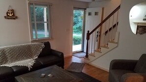 Una sala de estar con un sofá de color oscuro, una mesa de centro de madera y una escalera con barandilla de madera.