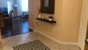 Un couloir orné d’un tapis à motifs, une étagère sombre fixée au mur et décorée d’objets, et une porte donnant sur une autre pièce.