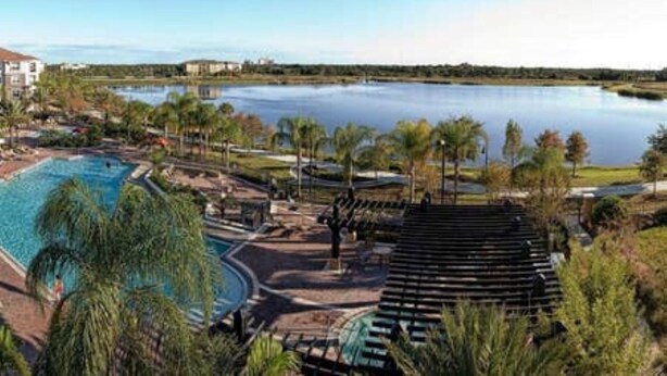 Un complexe hôtelier doté d’une grande piscine, offrant une vue sur un lac, et comprenant un espace couvert avec des marches.