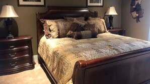 Quarto com cama de madeira, duas mesas de cabeceira com luminárias, cômoda e duas obras de arte emolduradas nas paredes.