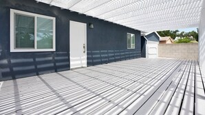 A covered outdoor deck with a dark wall and a white door. - Top-Rated 2BR Home · 5 Miles to Disneyland (Fullerton)