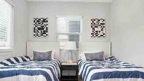 A bedroom with two beds, each with striped bedding, a nightstand, and a wall-mounted lamp. - Top-Rated 2BR Home · 5 Miles to Disneyland (Fullerton)