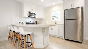 A modern kitchen with white cabinetry, a stainless steel refrigerator, and a central island with bar stools. - Top-Rated 2BR Home · 5 Miles to Disneyland (Fullerton)