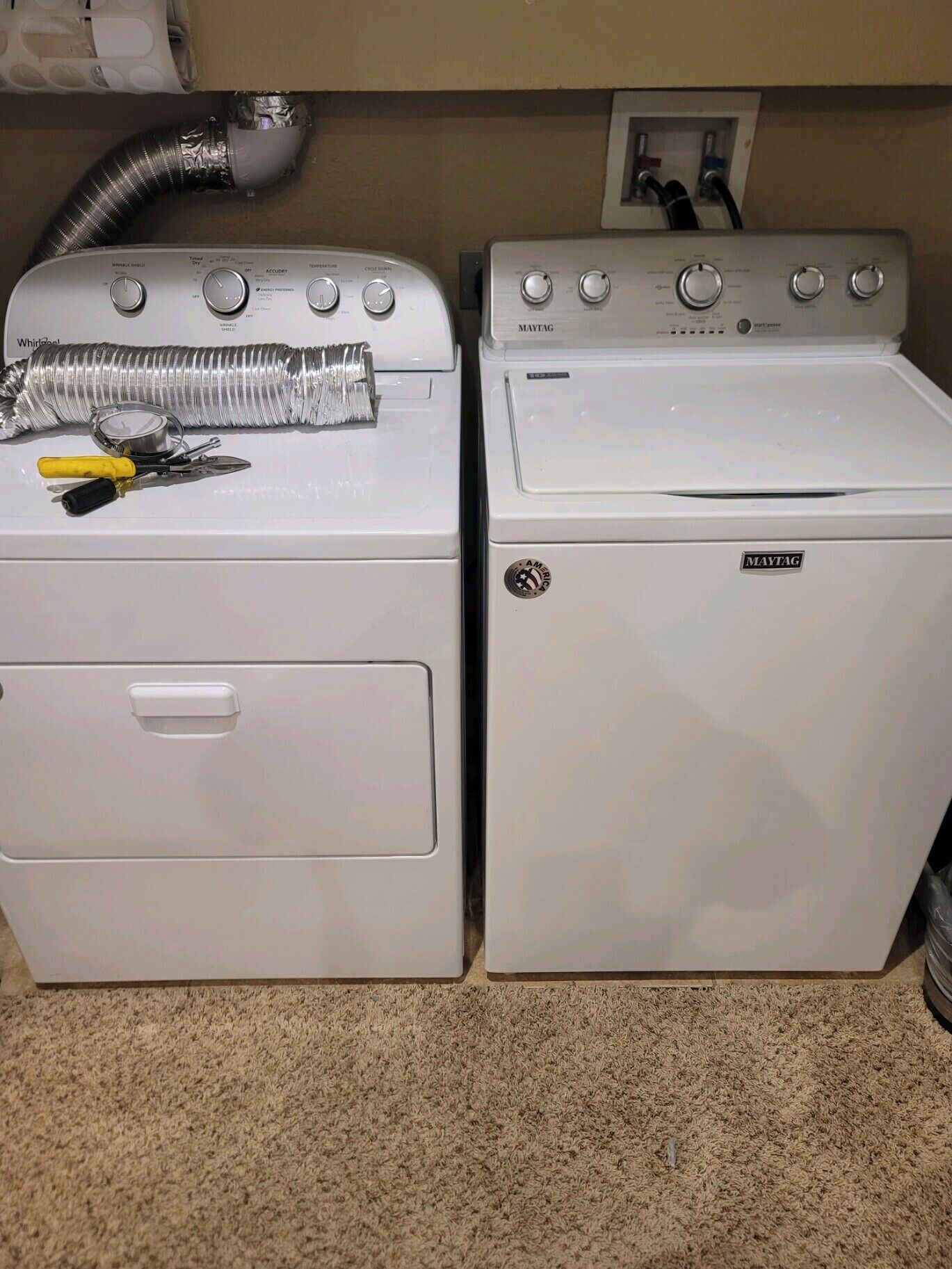Two white Maytag washing machines side by side with a vent hose and tools on the left one.