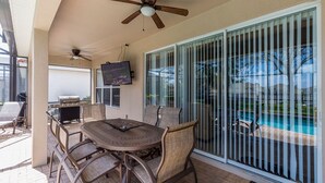 An outdoor patio with a round table, chairs, a ceiling fan, a TV, and a view of a swimming pool. - Windsor Orlando Arcade Room, Movie Theater, Pool & Hot Tub, King Bed, Bunk Bed (Kissimmee)