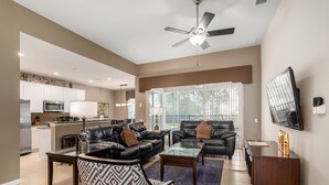 A spacious living area with a glass coffee table, two leather sofas, a patterned armchair, and a TV mounted on the wall. - Windsor Orlando Arcade Room, Movie Theater, Pool & Hot Tub, King Bed, Bunk Bed (Kissimmee)