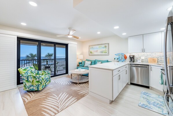 A modern kitchen with white cabinets, a dishwasher, and a dining area with a round table and teal sofa. - OCEAN'S REACH 1B4, 1-Bedroom, Top-Floor, Beautiful View, All Amenities Open! (Sanibel Island)