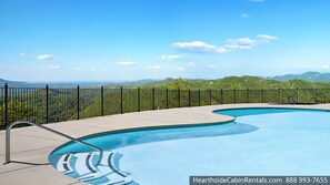 Une piscine au design incurvé, entourée d’une clôture en métal noir, et offrant une vue sur un paysage montagneux.