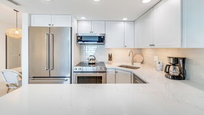 A modern kitchen with white cabinets, stainless steel appliances, and a marble countertop. - OCEAN'S REACH 2X4: 1-Bdrm, Top Floor/Gulf Front Unit! All Amenities Open! (Sanibel Island)