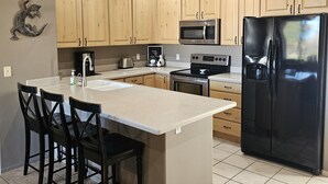 A kitchen with wooden cabinets, a black refrigerator, a microwave, and a sink. - Gated Golf Course Community Condo (St. George)