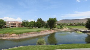 A golf course with a pond, a building with multiple windows, and a hilly landscape in the background. - Gated Golf Course Community Condo (St. George)